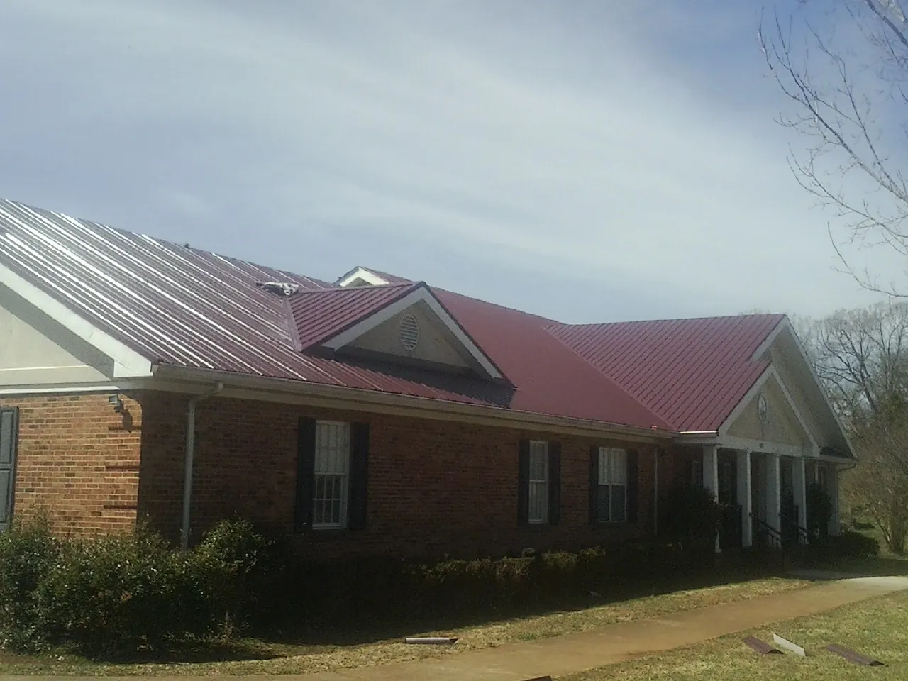Red metal roof with gabled entries on a long brick building, from a Hail Damage Roof Repair job in Pittsfield