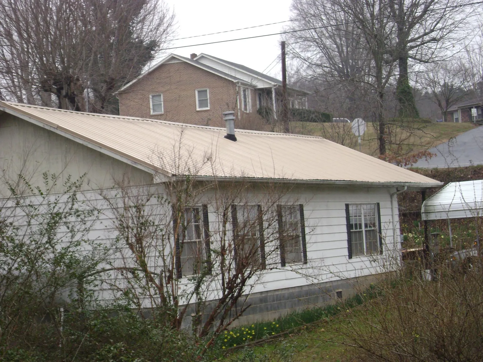 Tan metal roof on a white sided house set into a hillside — Commercial Roofing by Roofing Brothers in Pittsfield